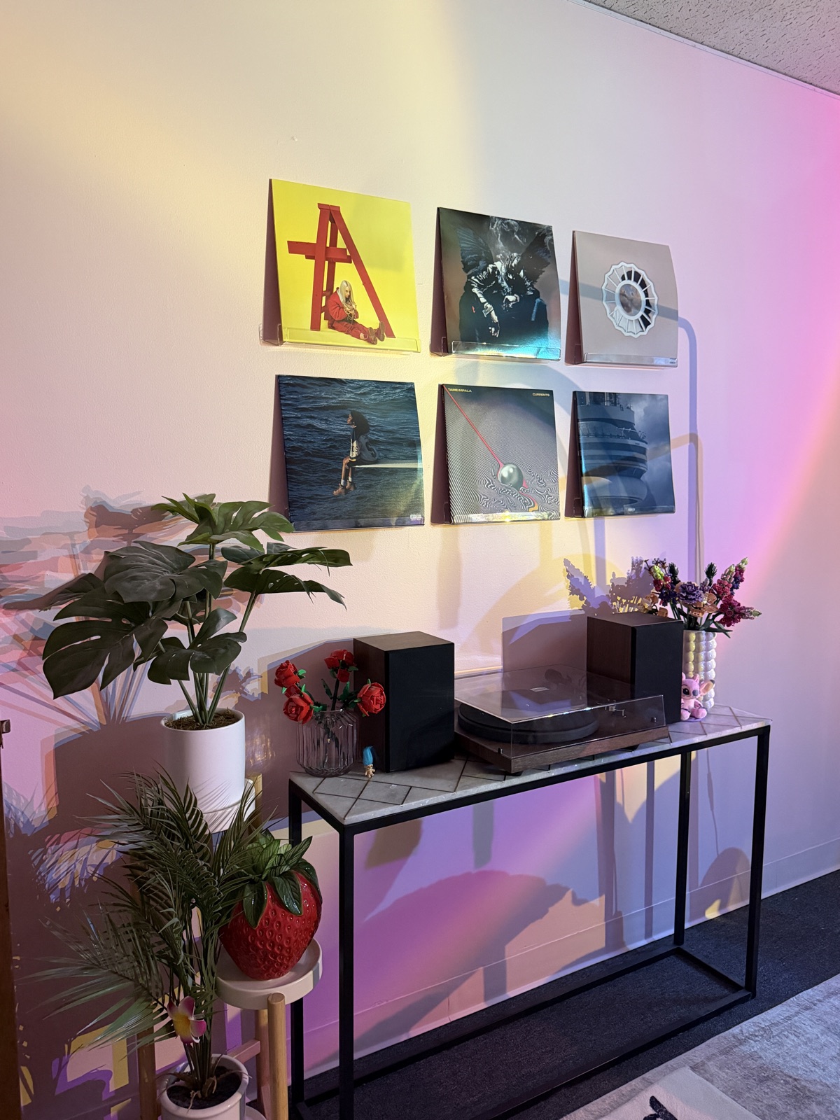 Records on the wall above a record player, with plants and red roses